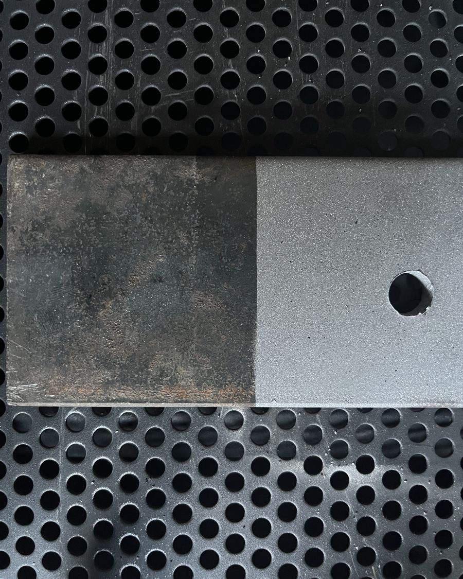 Flachstahl auf dem Gitterrost der Strahlkabine: links rostig wie angeliefert, rechts gestrahlt und metallisch sauber