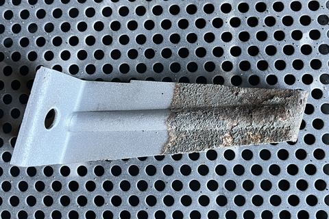 Stahlteil auf dem Gitterrost der Strahlkabine, links gestrahlt und hellgrau, rechts noch rostig